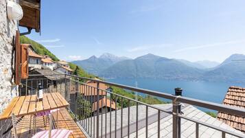 Ein Balkon mit Holztisch und -stühlen, mit Blick auf eine Berglandschaft und einen See.