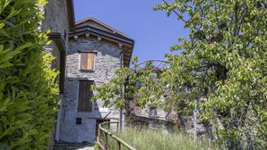 Un edificio de piedra con puerta y ventana de madera, rodeado de follaje y una valla de madera.