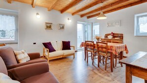 Una sala de estar acogedora con techo de madera, un sofá, una mesa de comedor con sillas y un ventanal con vistas.