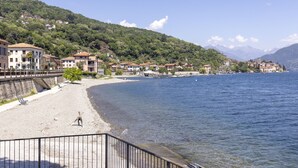 Un pueblo a orillas de un lago, con edificios a lo largo de la costa, una playa de arena y montañas al fondo.