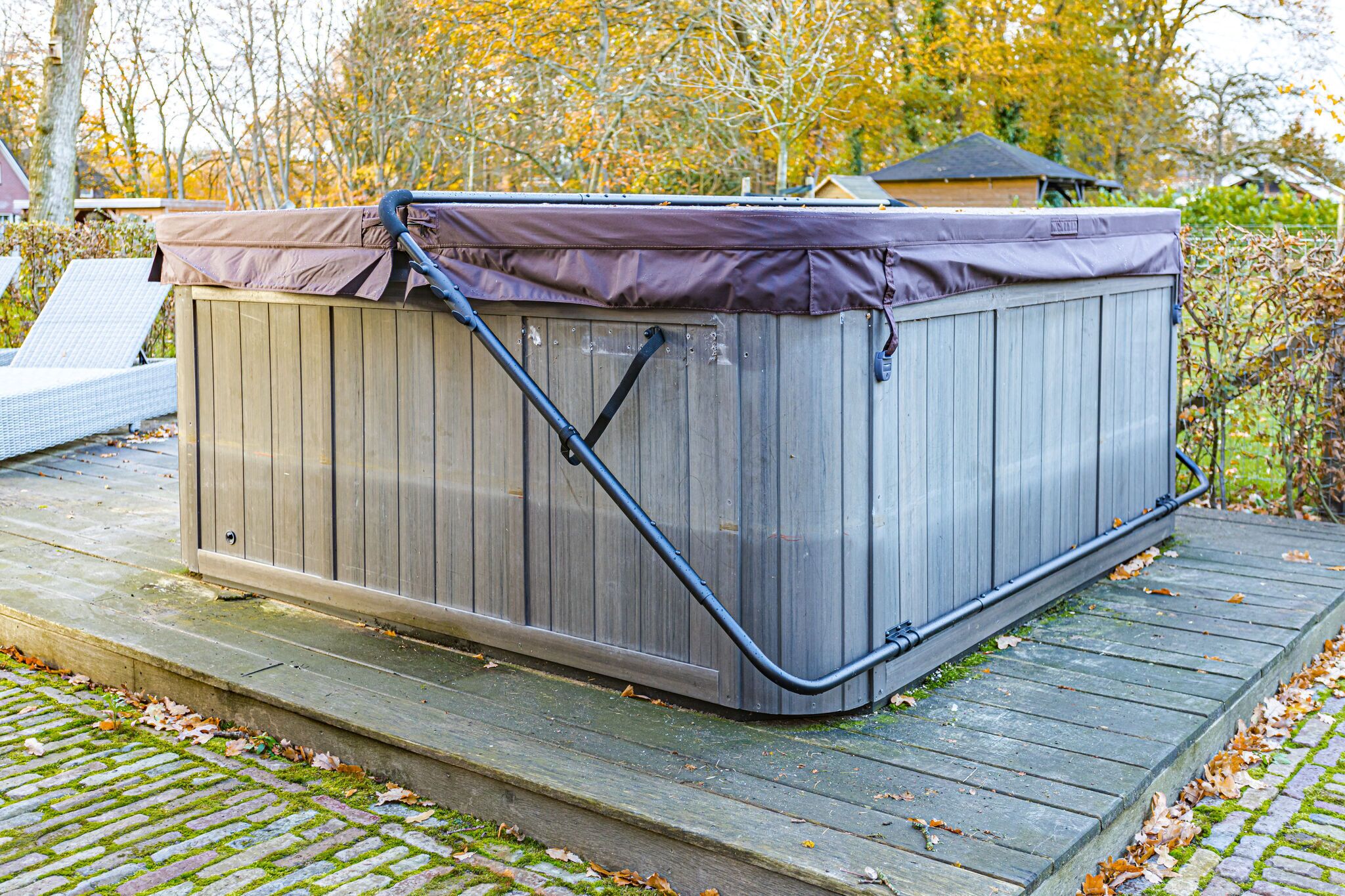 A hot tub on a wooden deck with a metal frame, surrounded by trees and a house in the background.