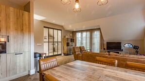 A modern living room with a large wooden dining table, leather sofas, and a TV. - Farmhouse Nijverdal near Sallandse Heuvelrug (Nijverdal)