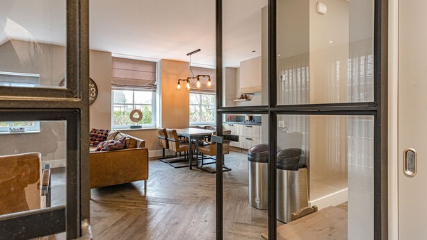 A modern kitchen with a central island, a dining area with a wooden table and chairs, and a cozy seating area with a sofa and cushions. - Farmhouse Nijverdal near Sallandse Heuvelrug (Nijverdal)