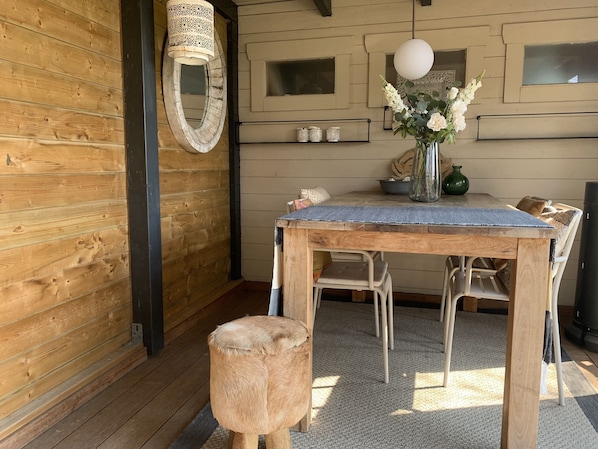Ein Holzinterieur mit einem runden Spiegel, einem Tisch mit Stühlen, einer Vase mit Blumen und einer hängenden Leuchte.