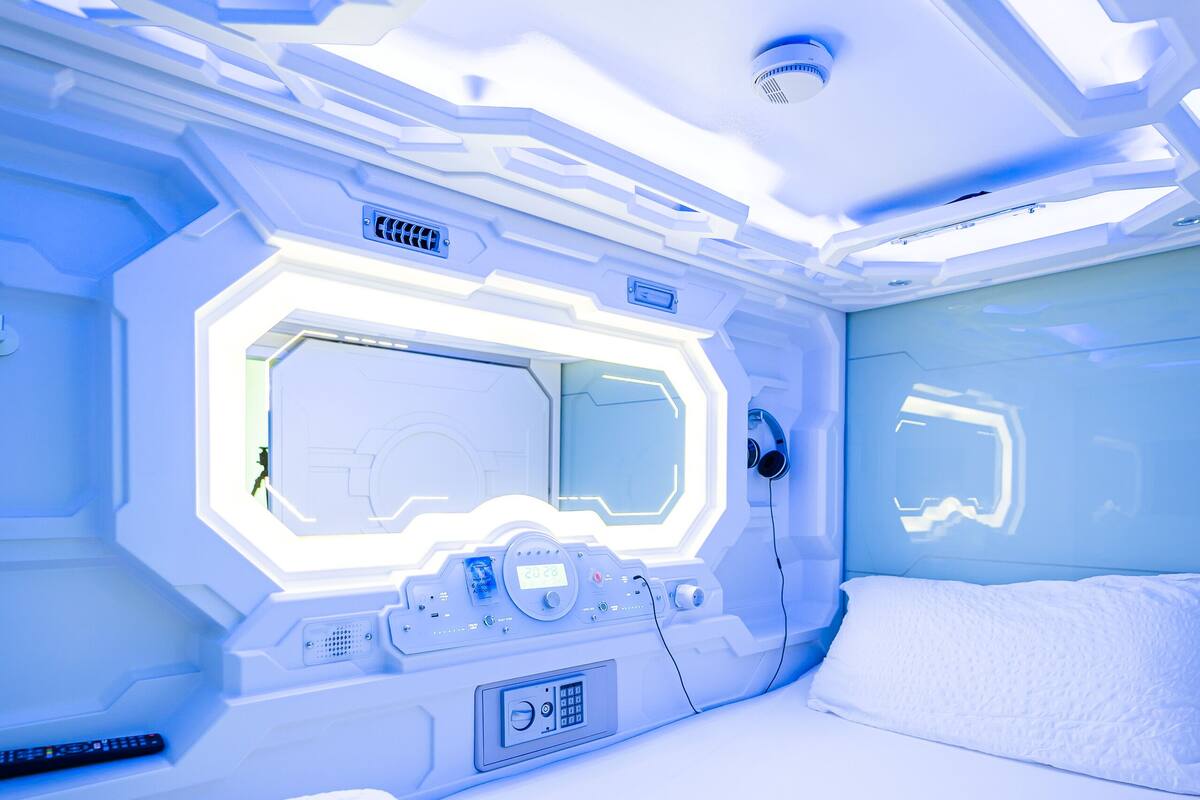 A futuristic room with a bed, a control panel, and a large window.
