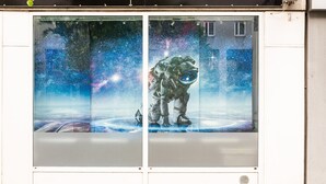 Un edificio con un letrero que dice "SPACE LHS 151" y grandes ventanas que exhiben arte con temática espacial.