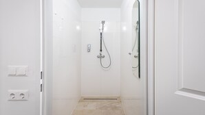 Un baño moderno con azulejos blancos, ducha con cabezal de ducha manual y un espejo.