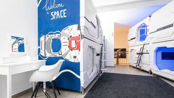 A room with a blue wall featuring a space-themed mural, a white desk with a chair, and two large, futuristic-looking beds.