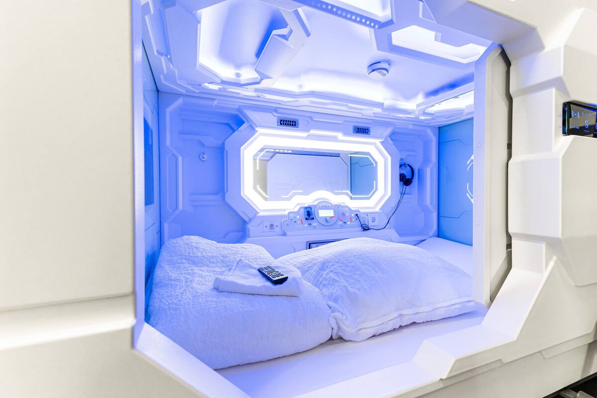 A futuristic room with a bed, a control panel, and a window.