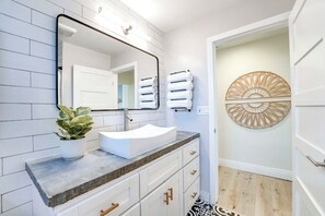 Une salle de bain avec un lavabo blanc, une plante en pot et un élément décoratif mural.