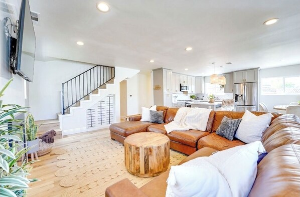 A spacious living room with a brown leather sofa, a wooden coffee table, and a staircase leading to an upper floor.