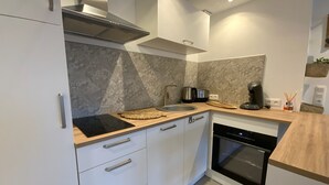 A modern kitchen with white cabinets, a stainless steel range hood, a built-in oven, and a wooden countertop. - Gîte with private Jacuzzi (St martin choquel)