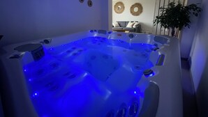 A modern bathroom with a large, illuminated bathtub, a wall-mounted toilet, and a potted plant. - Gîte with private Jacuzzi (St martin choquel)