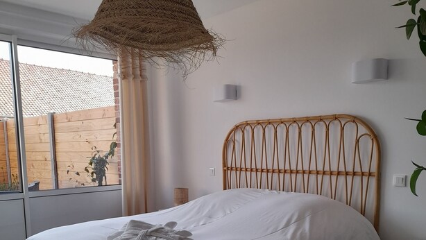 A bedroom with a bed, a woven ceiling light, a bedside table, a potted plant, and a view of the outside. - Gîte with private Jacuzzi (St martin choquel)
