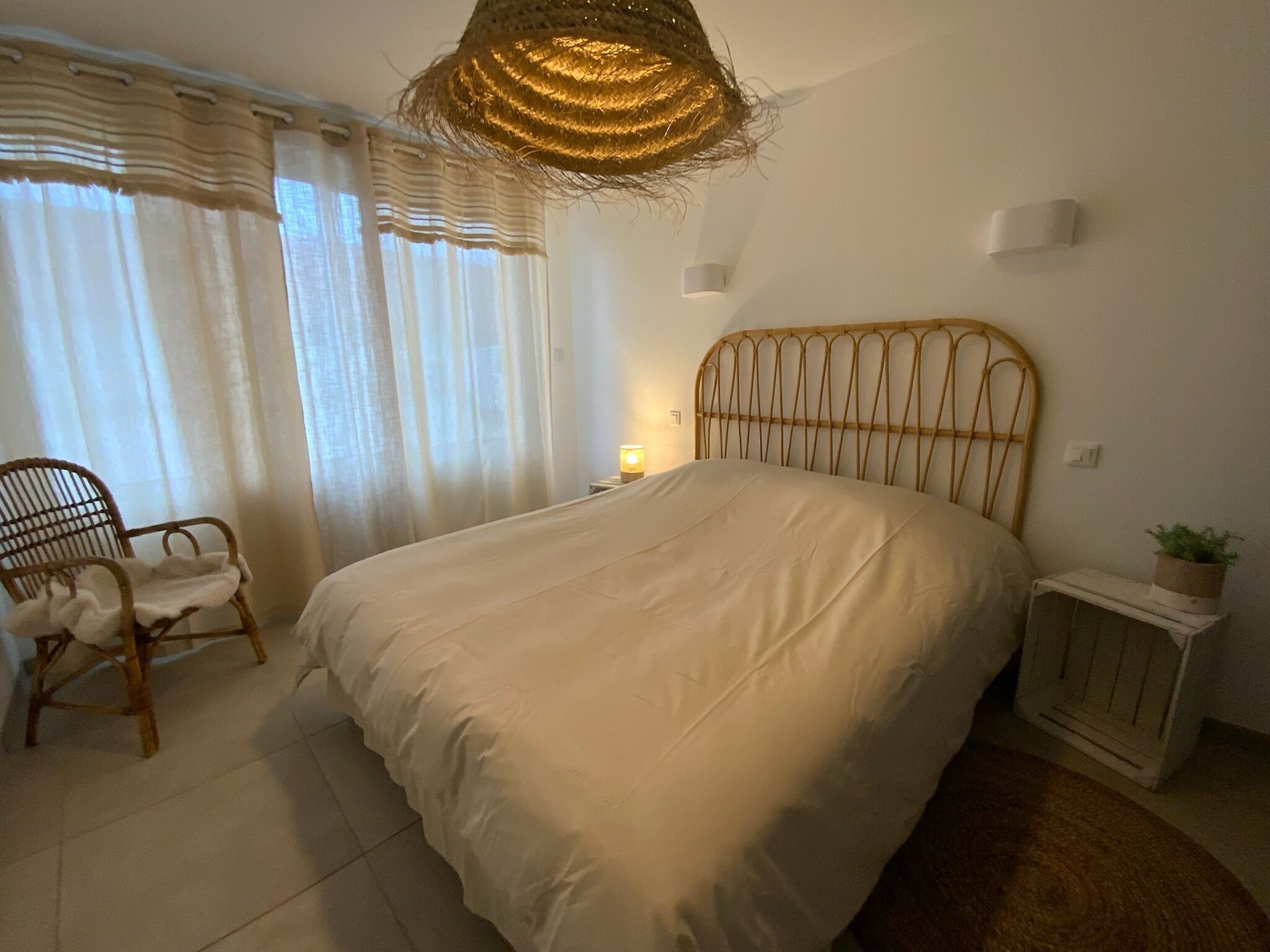 Un dormitorio con cama, una silla, una mesita de noche con lámpara y una lámpara colgante.