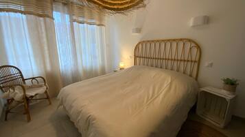 Un dormitorio con cama, una silla, una mesita de noche con lámpara y una lámpara colgante.