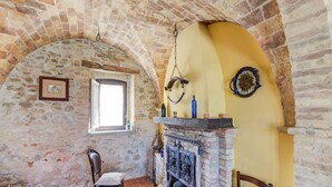 A rustic room with a stone wall, a fireplace, a wooden chair, and a window.