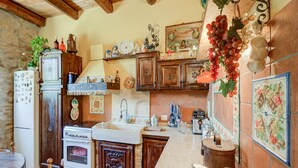 A rustic kitchen with wooden cabinets, a stone wall, and a tiled backsplash.