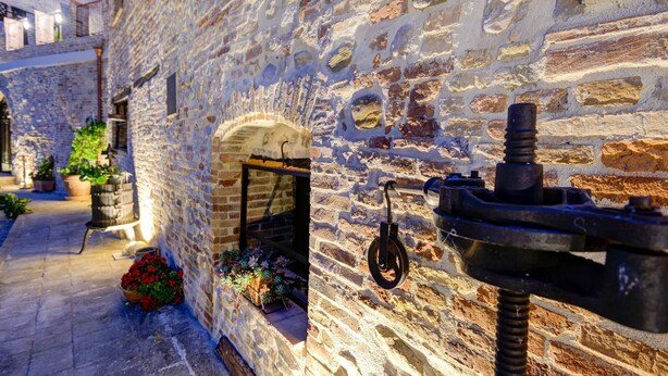 A narrow street with stone buildings, a visible archway, and potted plants.
