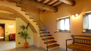 A spacious interior with a wooden staircase, a large potted plant, a bench, and a window with curtains. - Holiday Home in Urbania with Hill Views (Urbania)