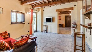 A cozy living area with a leather sofa, wooden beams, a TV, and a dining area with a table and chairs. - Holiday Home in Urbania with Hill Views (Urbania)