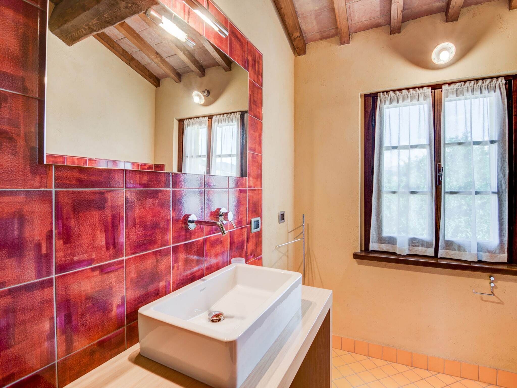 A bathroom with a white sink, red-tiled walls, a wooden ceiling, and a window with curtains.