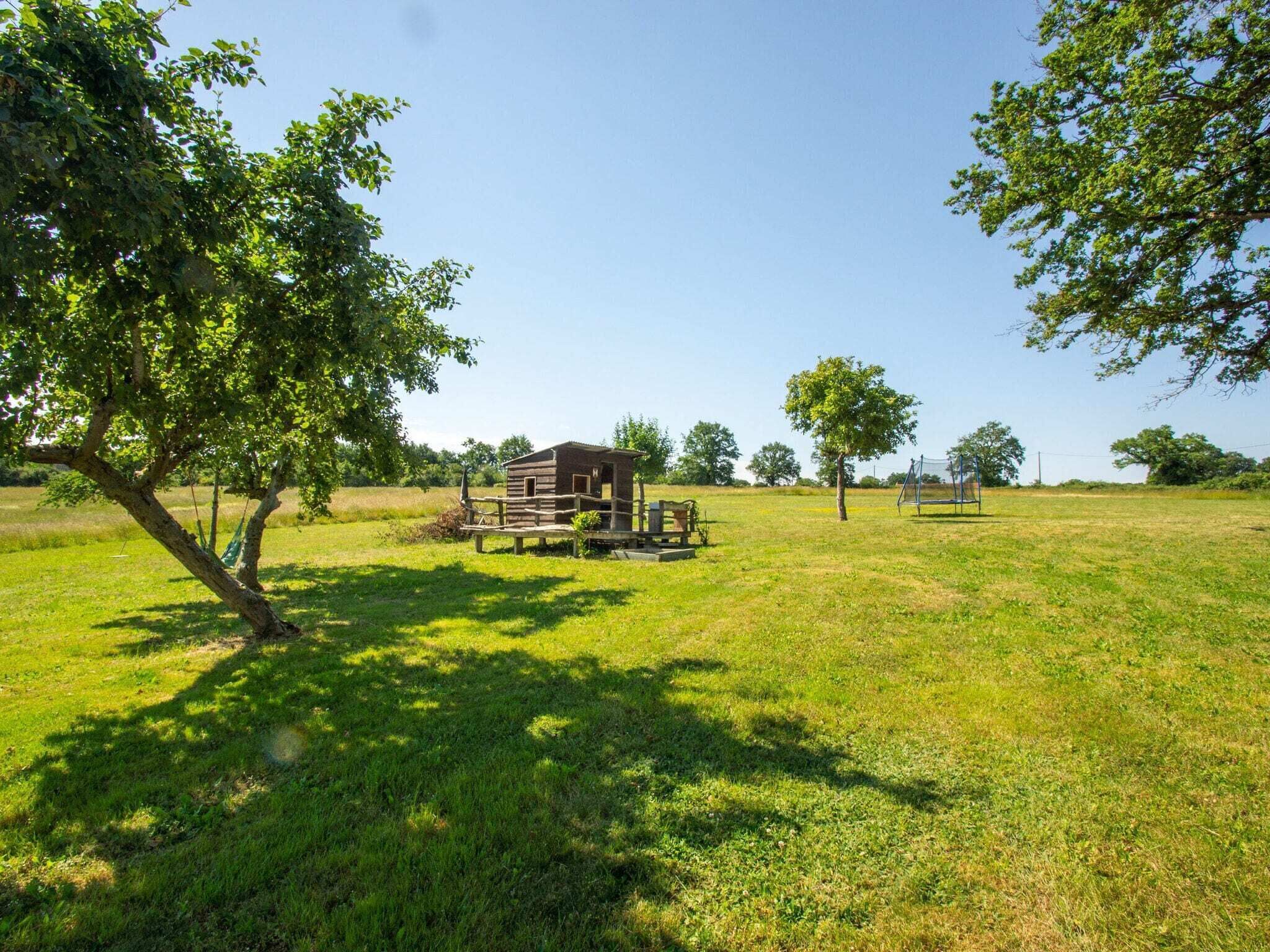 A rustic cabin in a grassy field with a wooden deck and a swing set.