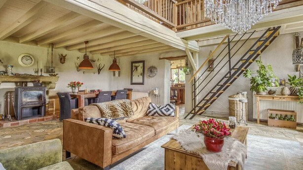 Un loft spacieux avec de hauts plafonds, des poutres apparentes, un magnifique lustre, un escalier et un coin salon confortable agrémenté d’une cheminée.