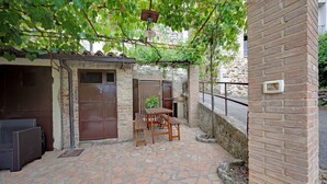 A patio with stone flooring, a wooden table and chairs, a wicker sofa, and a brick wall. - Mansion in Prodo near Lake Bolsena (Prodo)