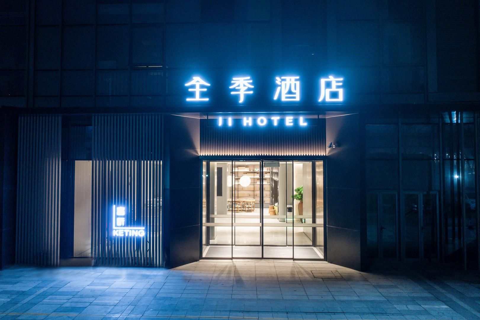 L’entrée d’un hôtel, avec une enseigne au néon, des portes en verre et une façade moderne.