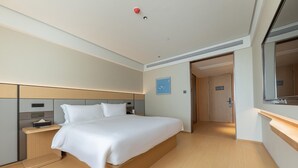 Une chambre d’hôtel moderne dotée d’un grand lit, de tables de chevet, d’une petite table, d’un miroir et d’une porte donnant accès à la salle de bain.