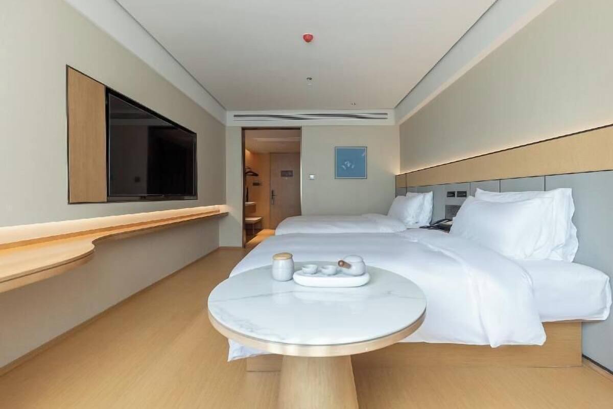 A hotel room with a bed, bedside table, and a TV on the wall.