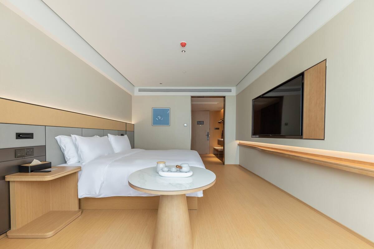 A hotel room with a bed, bedside table, bedside lamp, and a small round table with a tray.
