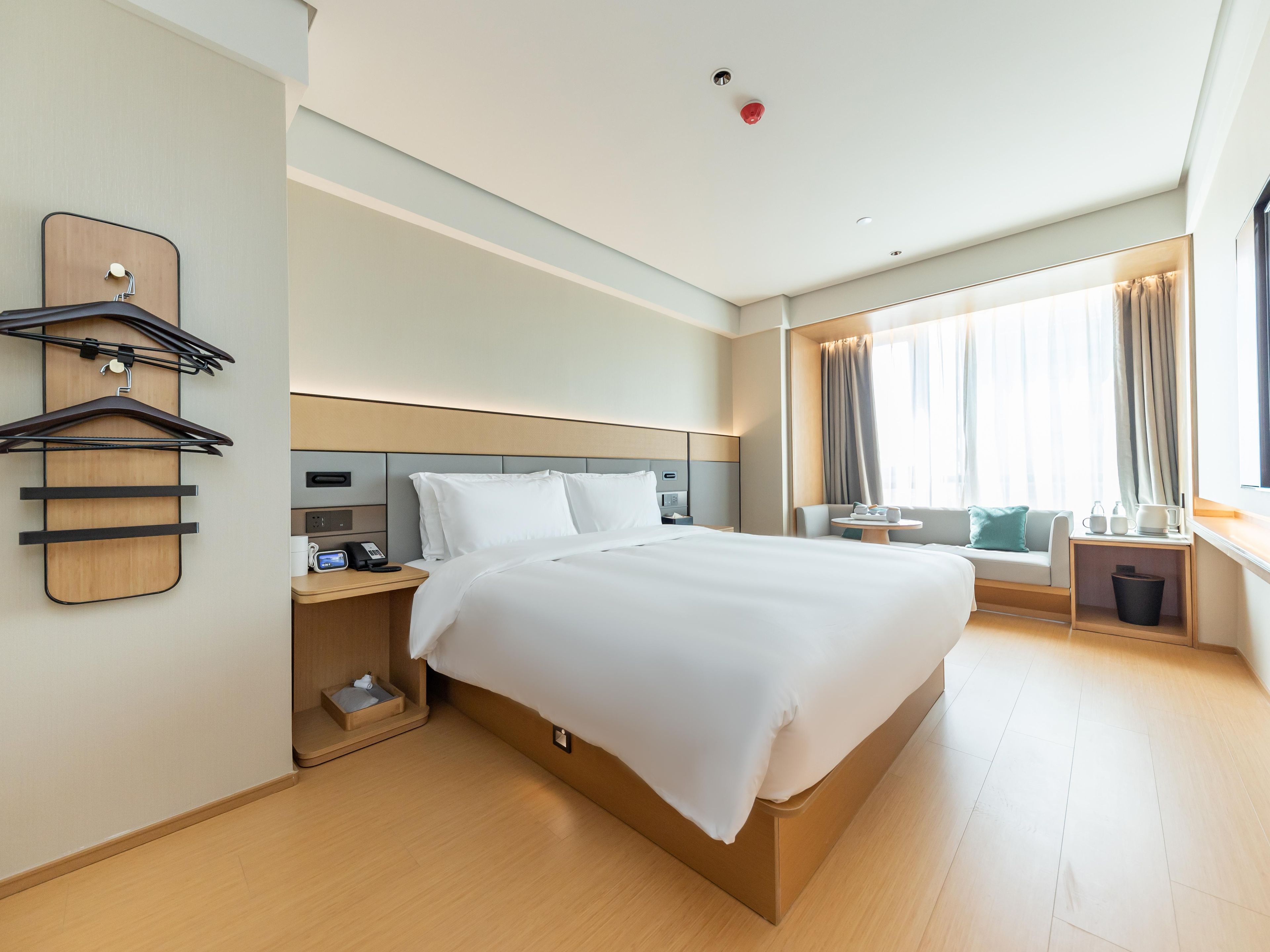 Quarto de hotel com uma cama grande, mesas de cabeceira, uma escrivaninha e uma janela com cortinas.