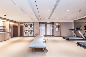 Una habitación de hotel moderna con una cama grande, un escritorio, una lavadora, una cinta de correr y una mesita.