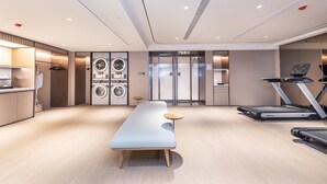 Une chambre d’hôtel moderne équipée d’un grand lit, d’un bureau, d’un lave-linge, d’un tapis de course et d’une petite table.