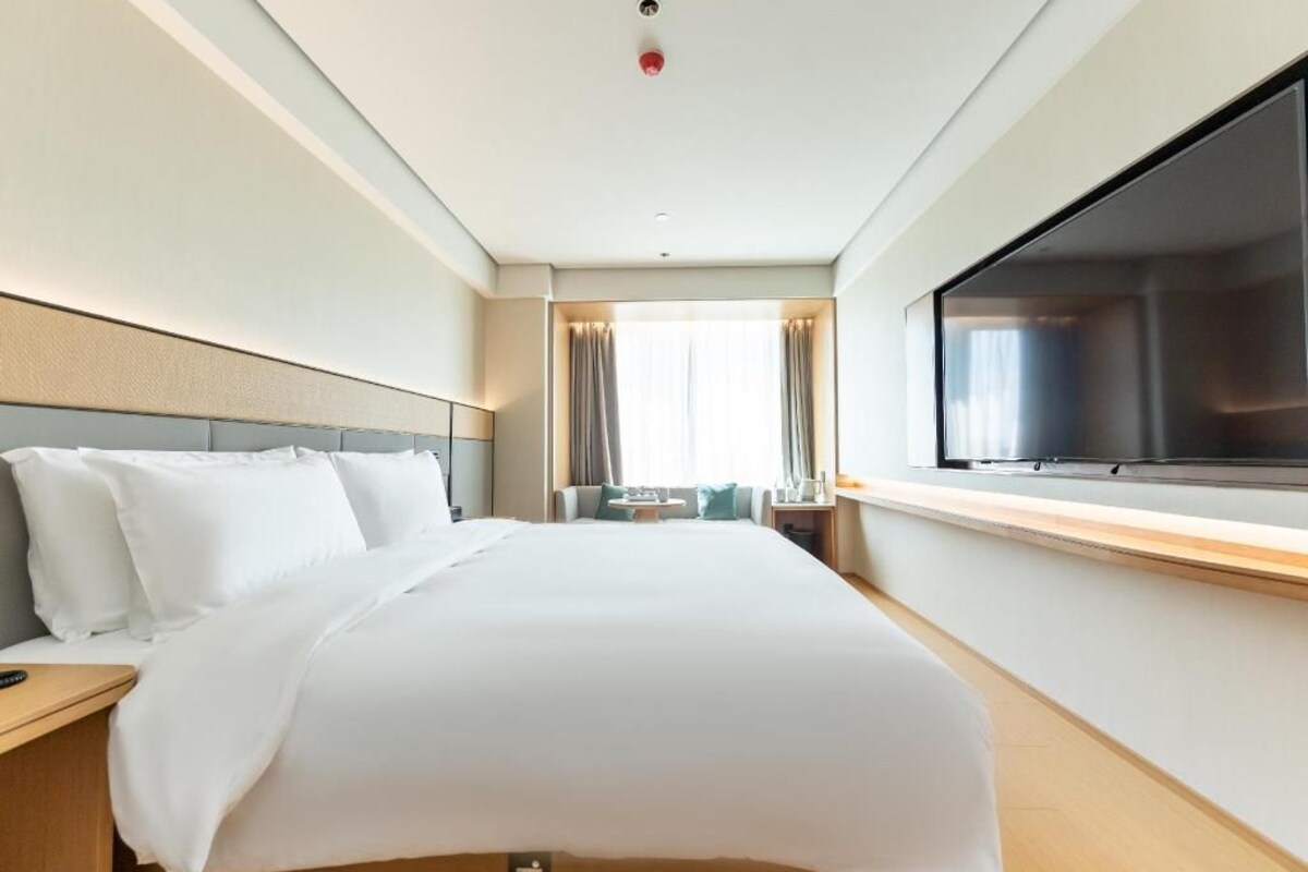 A hotel room with a large bed, a TV, a window with curtains, and a bedside table.