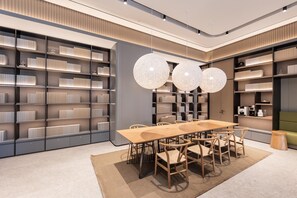 Un interior moderno con una larga mesa de comedor, múltiples sillas y una amplia estantería llena de libros.