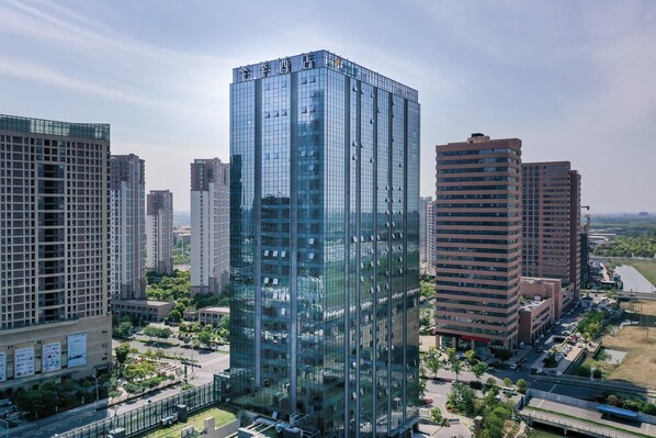 Un edificio alto con fachada de vidrio, rodeado de otros edificios, y un río al fondo.