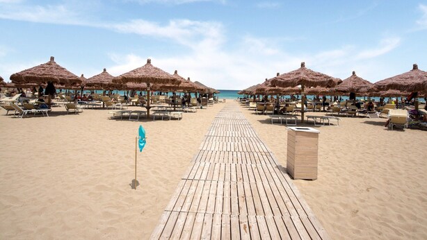A beach with thatched umbrellas and sun loungers, a wooden walkway, and a clear view of the sea.