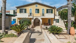 A two-story building with a central entrance, surrounded by palm trees and a paved courtyard.