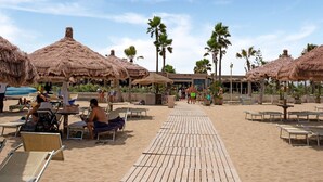 A beach with thatched umbrellas, sun loungers, and a wooden walkway.