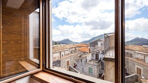 Une vue depuis une fenêtre donnant sur une ville historique, avec son architecture traditionnelle et des montagnes en arrière-plan.