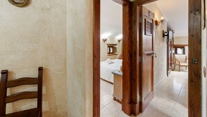 Un couloir menant à une chambre à coucher, où se trouvent un lit, une chaise en bois et une porte portant un numéro.