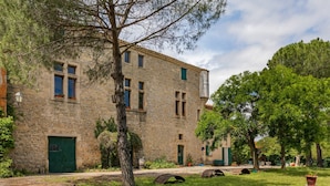A stone building with multiple windows and a green door, surrounded by a grassy area with trees and a clear sky. - Flat in a beautiful building with pool (Mèze)