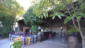 An outdoor bar area with wooden flooring, bar stools, and a rustic kitchen setup. - Flat in a beautiful building with pool (Mèze)