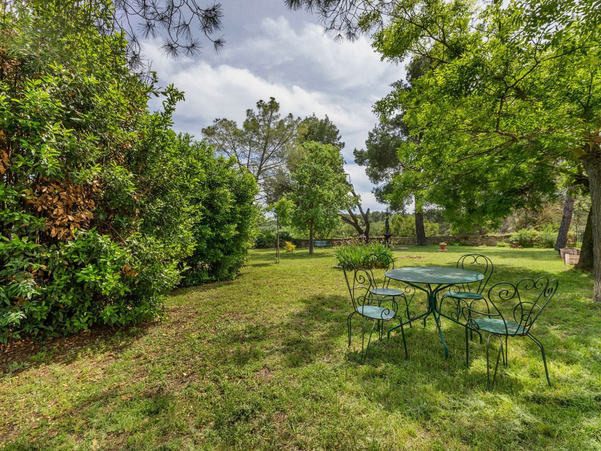 A lush garden with a metal table and chairs, surrounded by dense foliage and trees.