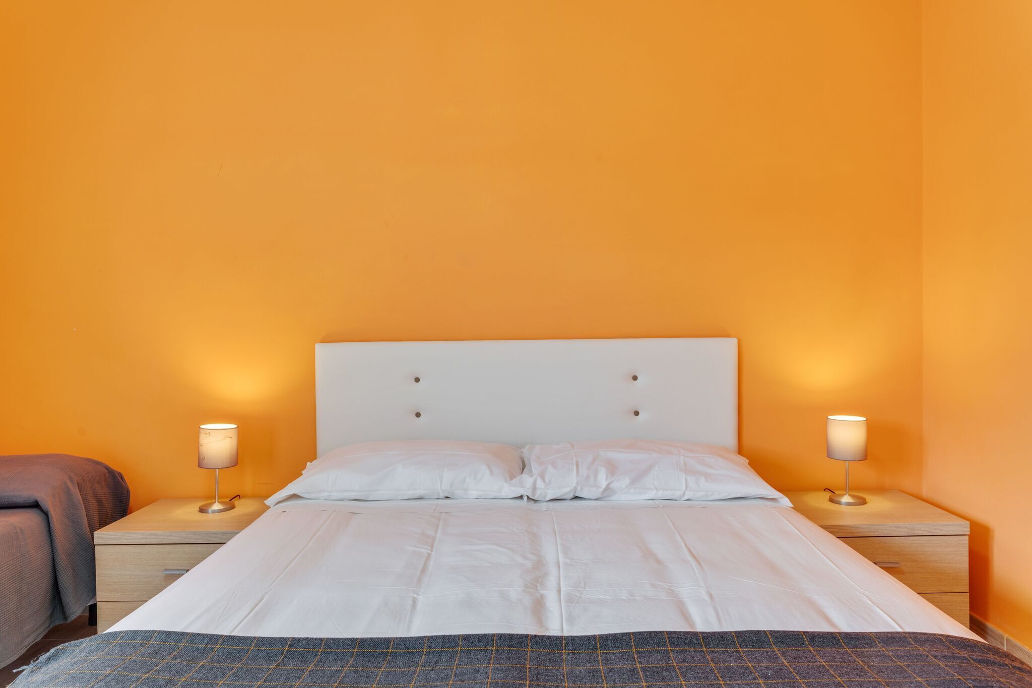 Un letto rifatto con lenzuola bianche, due comodini con lampade e una parete arancione.