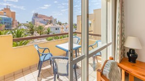 A balcony with a table and chairs, a lamp, and a view of buildings and palm trees. - Roquetas Beachside Getaway (Roquetas del Mar)
