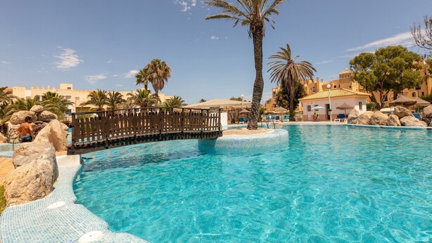 A clear blue pool with a wooden deck and palm trees, surrounded by buildings. - Roquetas Beachside Getaway (Roquetas del Mar)